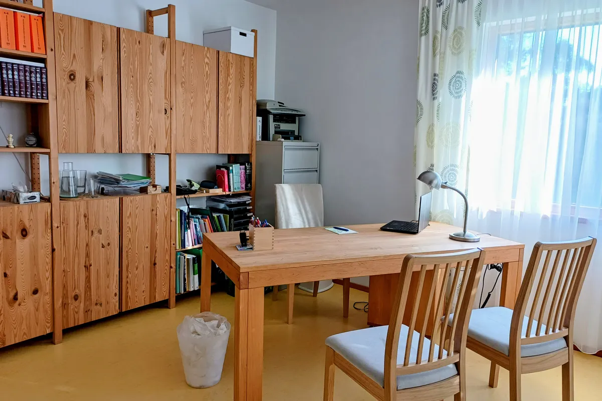 Ordinationszimmer mit Schreibtisch, Sesseln und Fenster – heller Raum mit Holzmöbeln